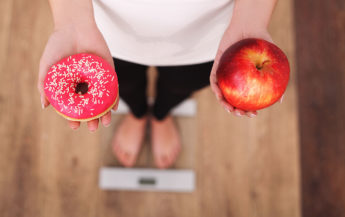 Woman on scale deciding between a donut or an apple